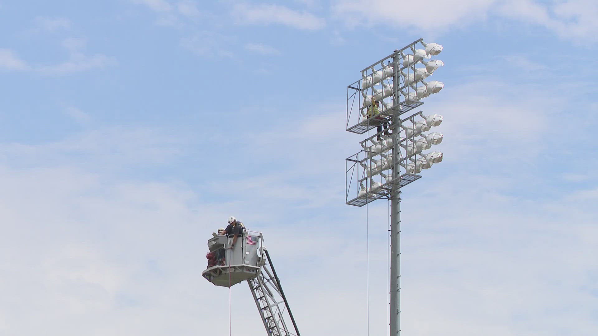 Firefighters ascend 120 feet up light pole to rescue injured worker at Mesa stadium.